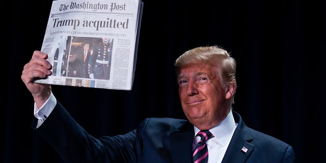 President Donald Trump holds up a newspaper with the headline that reads "Trump acquitted" during the 68th annual National Prayer Breakfast, at the Washington Hilton, Thursday, Feb. 6, 2020, in Washington. (AP Photo/ Evan Vucci)