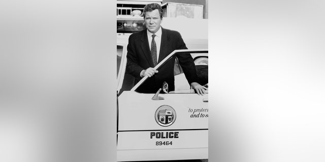 William Shatner stands behind the door of a police car as he hosts the CBS television true crime program 'Rescue 911'.