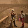 Two people dressed in carnival costumes stand beneath a cloud of red dust in Santa Cruz de Tenerife, Spain, Feb. 23, 2020. 