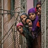 Indian Muslim women look out of a window as security officers patrol a street in New Delhi, India, Feb. 26, 2020. 