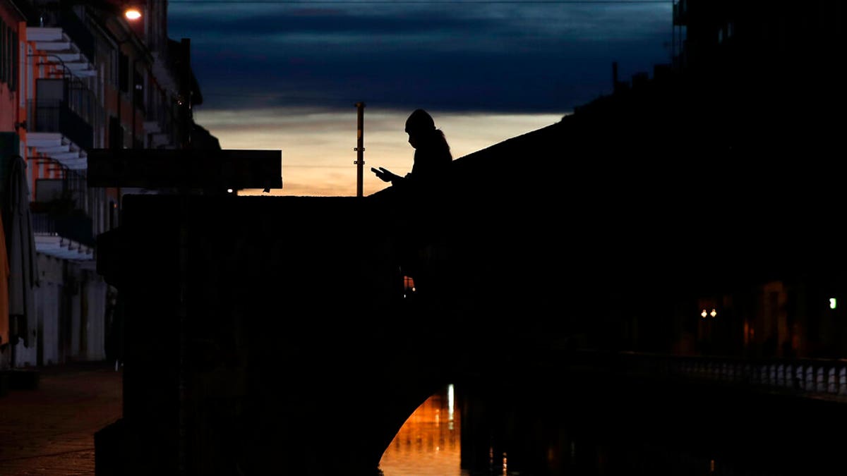 A woman wearing a face mask checks her phone as she walks at the Naviglio Grande canal in Milan, Italy. 