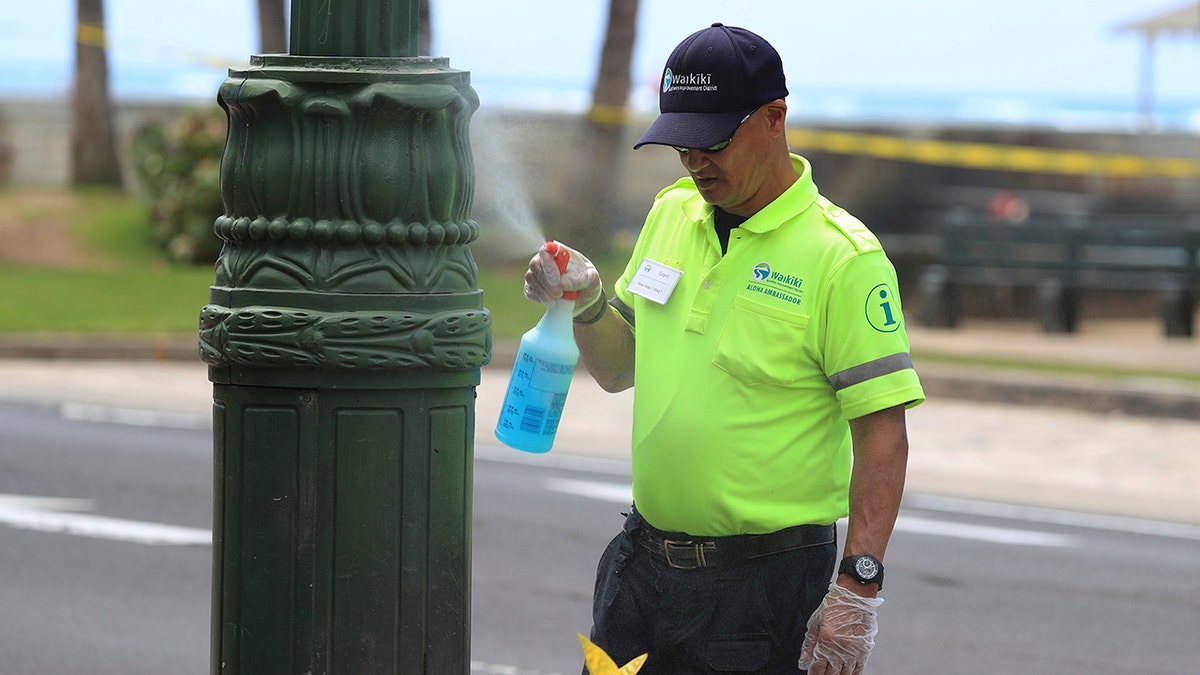 A worker sprays sanitizer on a light post Friday, March 20, 2020, in the Waikiki area of Honolulu. Honolulu closed all public parks and recreation areas Friday until the end of April in an effort to help stop the spread of the coronavirus.