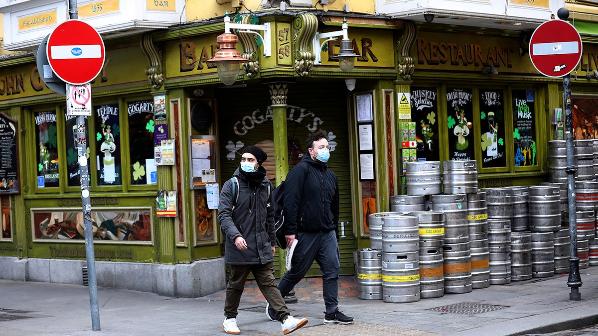 Tourists wearing face masks walk past a closed pub in Dublin city center, Monday, March, 16.