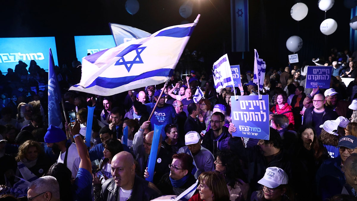 Blue and White party supporters hold banners and flags during an election campaign rally in Tel Aviv, Israel, Saturday. The Hebrew writing says, "Must to advance ". (AP Photo/Oded Balilty)