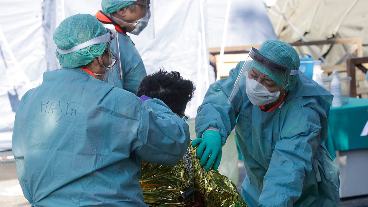 A man wrapped in a survival blanket is assisted by medical staff upon his arrival at one of the emergency structures that were set up to ease procedures at the Brescia hospital, Italy, Monday, March 16, 2020.