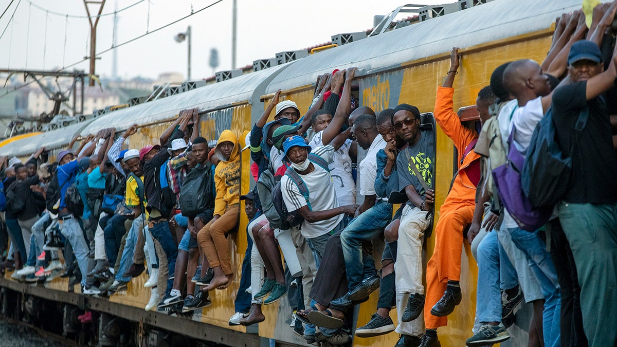 Train commuters hold on to the side of an overcrowded passenger train in Soweto, South Africa, Monday, March 16, 2020. South Africa will revoke nearly 10,000 visas issued this year to people from China and Iran, and visas will now be required for other high-risk countries that had been visa-free, including Italy and the United States. (AP Photo/Themba Hadebe)
