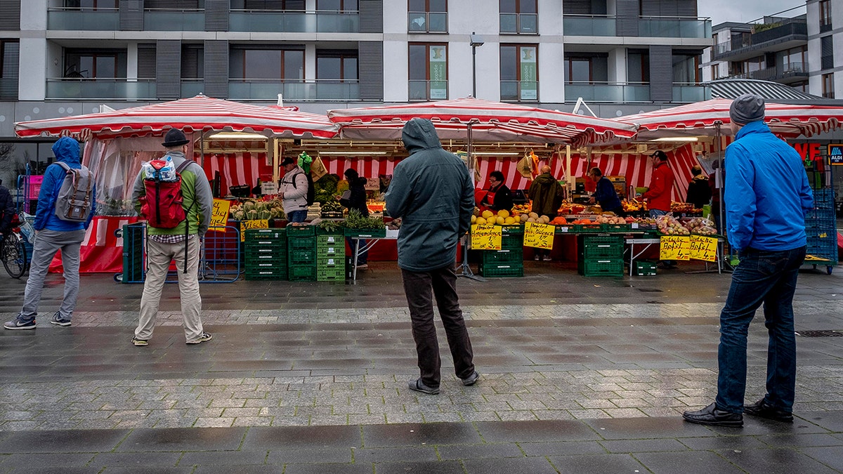 People keep distance as they queue on a small weekly market in Frankfurt, Germany, early Saturday, March 21, 2020.