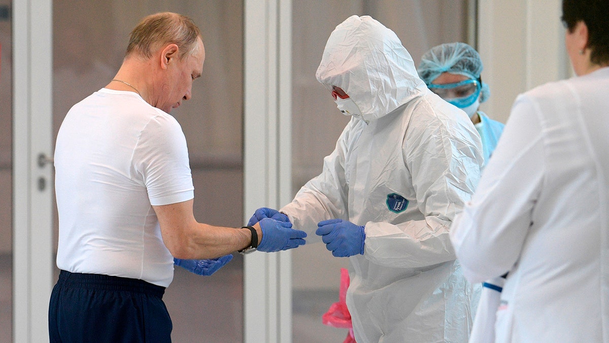 Russian President Vladimir Putin, left, dons gloves during his visit to the hospital for coronavirus patients in Kommunarka settlement, outside Moscow, Russia, Tuesday, March 24, 2020.