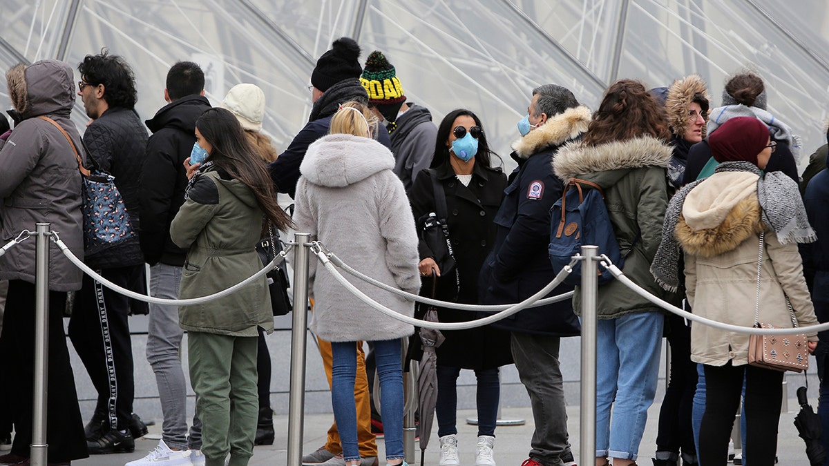 Tourists, some wearing a mask, queue to enter the Louvre museum Friday, Feb. 28, 2020 in Paris. The world is scrambling to get on top of the new coronavirus outbreak that has spread from its epicenter in China to most corners of the planet. (AP Photo/Rafael Yaghobzadeh)