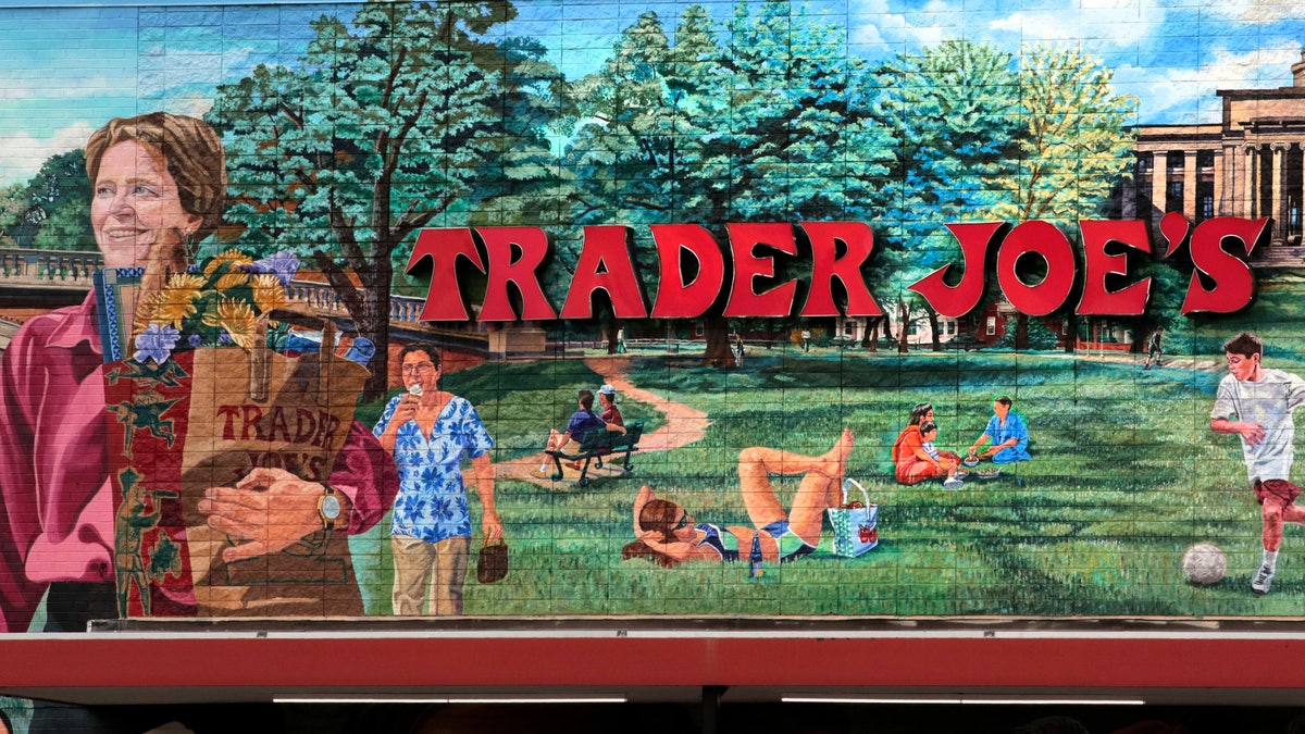 FILE - In this Aug. 13, 2019, file photo, Trader Joe's logo hangs on a mural at it's market in Cambridge, Mass.. The man who created Trader Joe's markets with a vision that college-educated but poorly paid young people would buy healthy foods if they could only afford them has died. Joe Coulombe's family says he died Friday at age 89. (AP Photo/Charles Krupa)