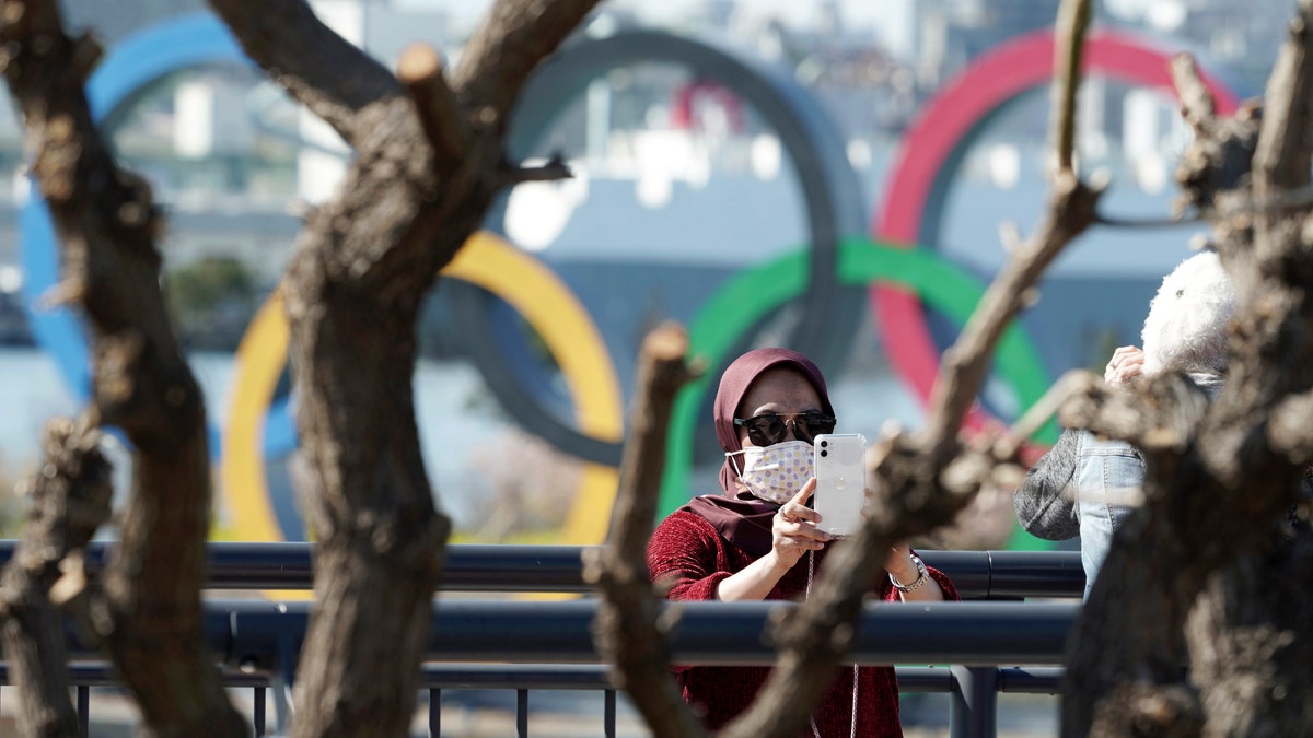 A tourist wearing a protective mask takes a photo with the Olympic rings in the background Tuesday, March 3, 2020, at Tokyo's Odaiba district. The spreading virus from China has put the Tokyo Olympics at risk. The Olympics are to open on July 24 - less than five months away. (AP Photo/Eugene Hoshiko)