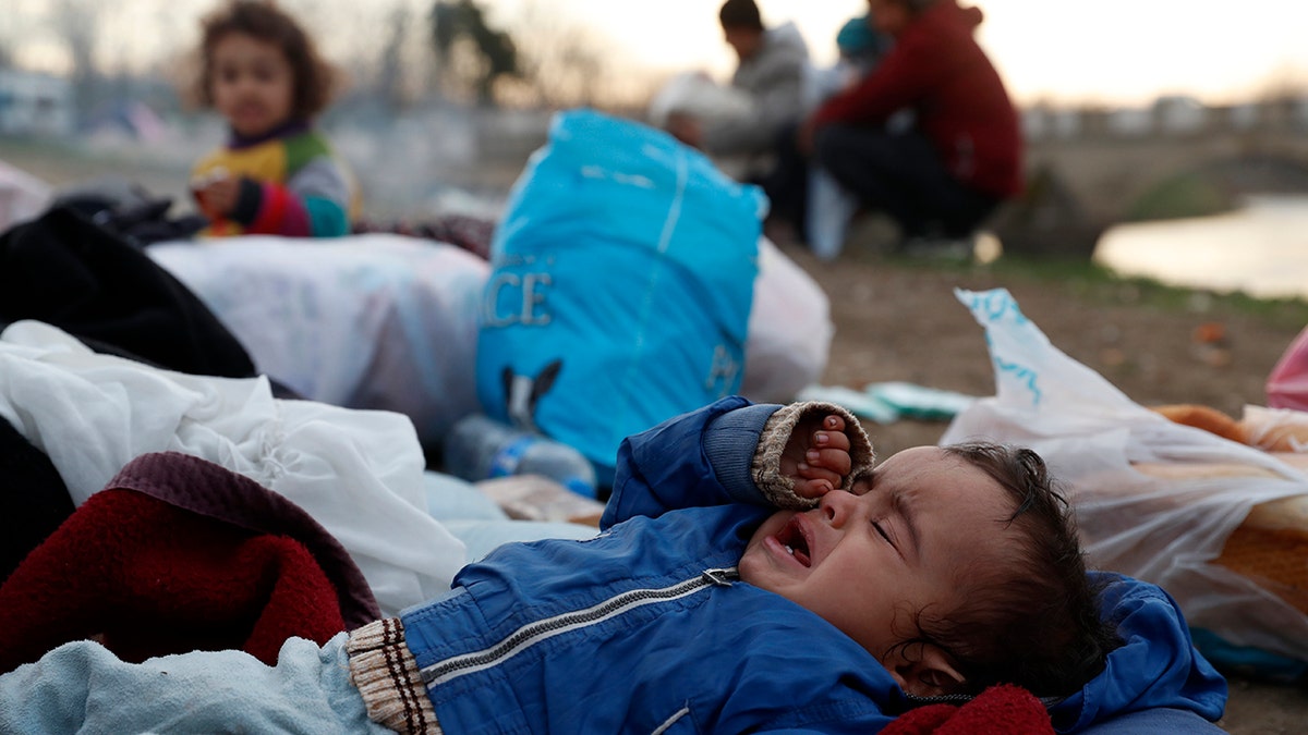 A baby cries as migrants gather next to a river in Edirne, Turkey, near Turkish-Greek border on Wednesday, March 4, 2020. Facing a potential wave of nearly a million people fleeing fighting in northern Syria, Turkey has thrown open its borders with Greece to thousands of refugees and other migrants trying to enter Europe, and has threatened to send "millions" more. (AP Photo/Darko Bandic)