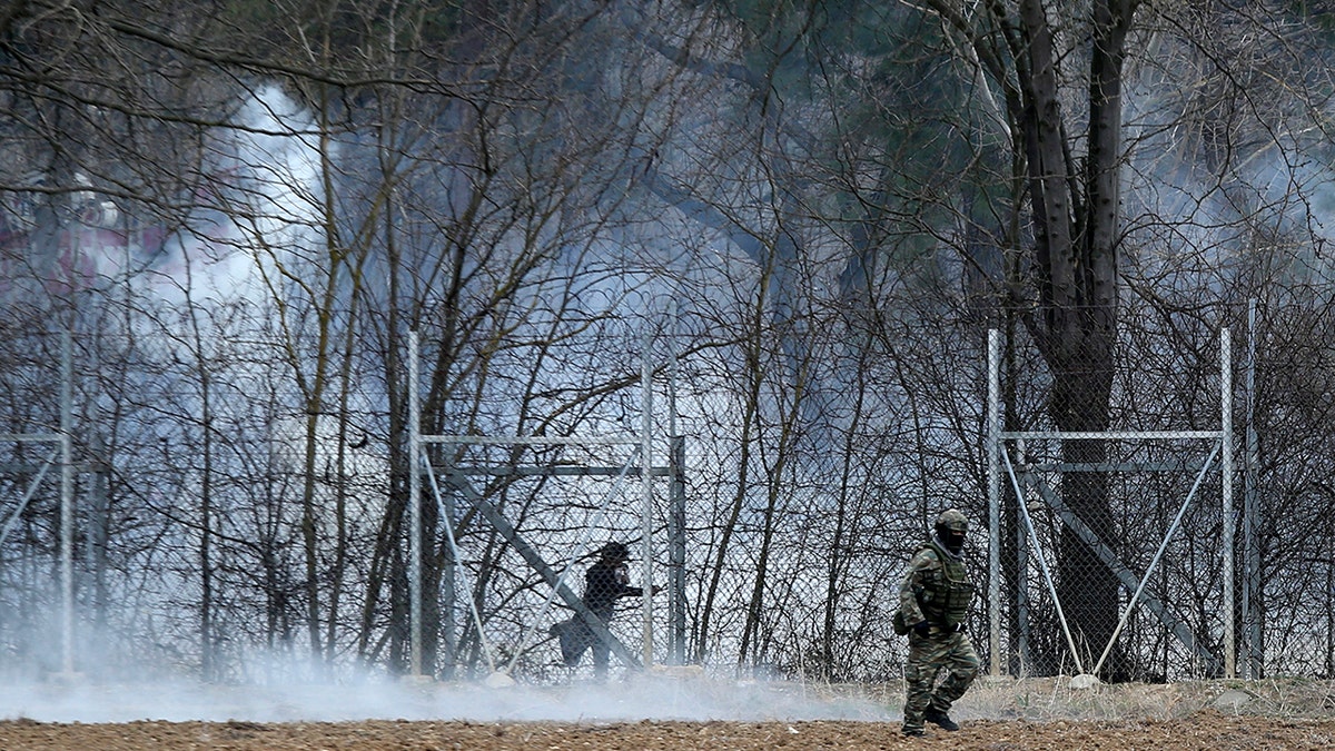 A Greek army officer patrols as a migrant is seen at the Turkish side at the Greek-Turkish border in Kastanies on Wednesday, March 4, 2020. Facing a potential wave of nearly a million people fleeing fighting in northern Syria, Turkey has thrown open its borders with Greece to thousands of refugees and other migrants trying to enter Europe, and has threatened to send "millions" more. (AP Photo/Giannis Papanikos)