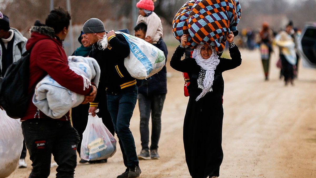 A woman carries her belongings as she walks with other migrants at the Turkish-Greek border in Pazarkule on Wednesday, March 4, 2020. Greek authorities fired tear gas and stun grenades Wednesday morning to repulse a push by migrants to cross its land border from Turkey, as pressure continued along its frontier after Turkey said its own border with Europe was open to whoever wanted to cross. (AP Photo/Emrah Gurel)