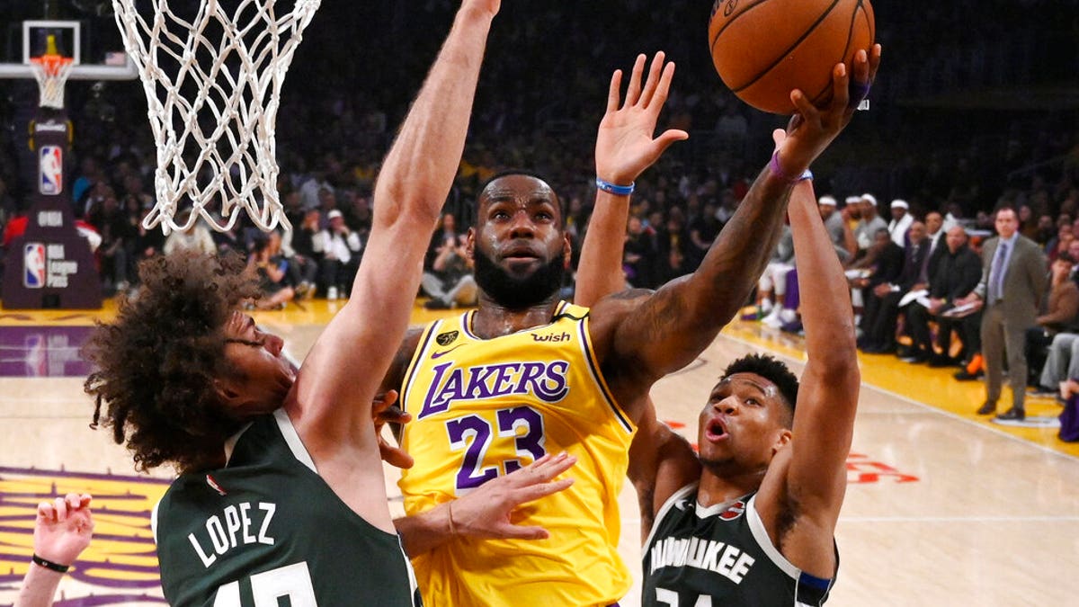 Los Angeles Lakers forward LeBron James, center, shoots as Milwaukee Bucks center Robin Lopez, left, and forward Giannis Antetokounmpo defend during the first half of an NBA basketball game Friday, March 6, 2020, in Los Angeles.
