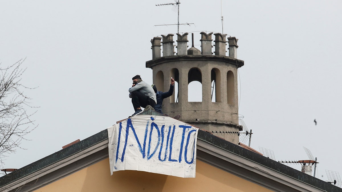 Inmates stand by a banner reading in Italian Pardon as they stage a protest against new rules to cope with coronavirus emergency, including the suspension of relatives' visits, on the roof of the San Vittore prison in Milan, Italy, Monday, March 9, 2020. (AP Photo/Antonio Calanni)