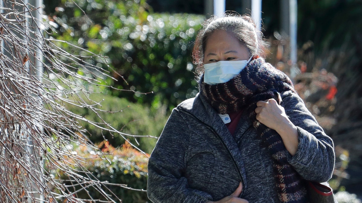 A worker at the Life Care Center in Kirkland, Wash., wears a mask and a scarf as she walks away from the facility, Monday, March 9, 2020, near Seattle. (AP Photo/Ted S. Warren)