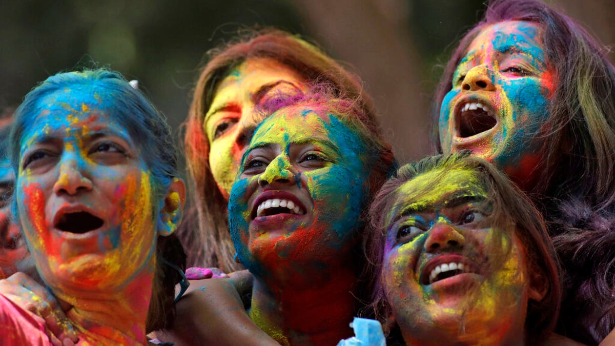 Women with their faces smeared with colored powder cheer during celebrations marking the Holi festival in Mumbai, India, Tuesday, March 10, 2020. 