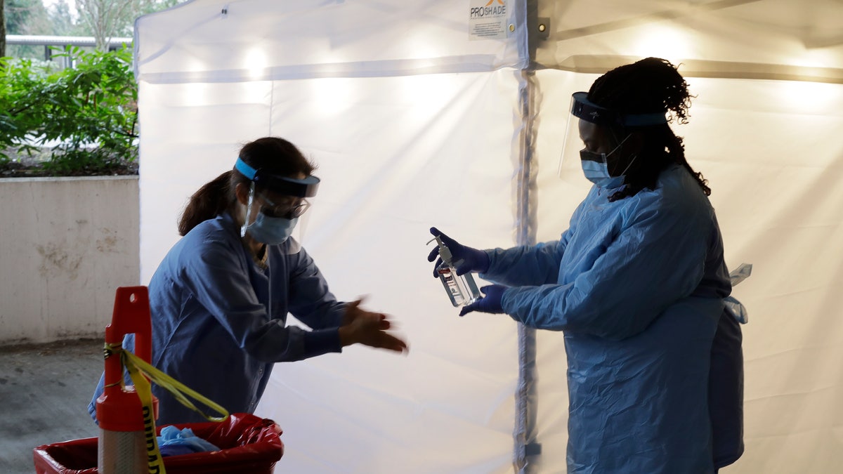 Nurses at a drive-up coronavirus testing station set up by the University of Washington Medical Center sanitize their hands after taking a nose swab sample from a person in a car Friday, March 13, 2020, in Seattle.  (AP Photo/Ted S. Warren)