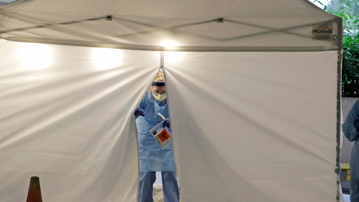 A nurse at a drive-up COVID-19 coronavirus testing station set up by the University of Washington Medical Center exits a tent while holding a bag containing a swab used to take a sample from the nose of a person in their car, Friday, March 13, 2020, in Seattle.