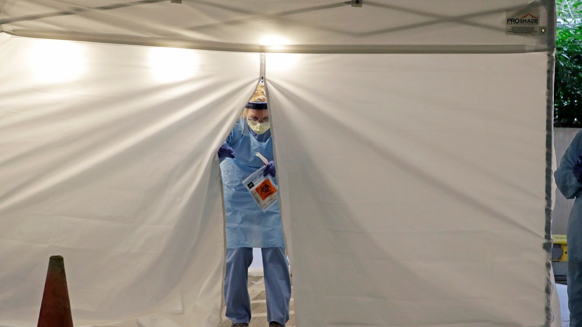 A nurse at a drive-up COVID-19 coronavirus testing station set up by the University of Washington Medical Center exits a tent while holding a bag containing a swab used to take a sample from the nose of a person in their car, Friday, March 13, 2020, in Seattle.