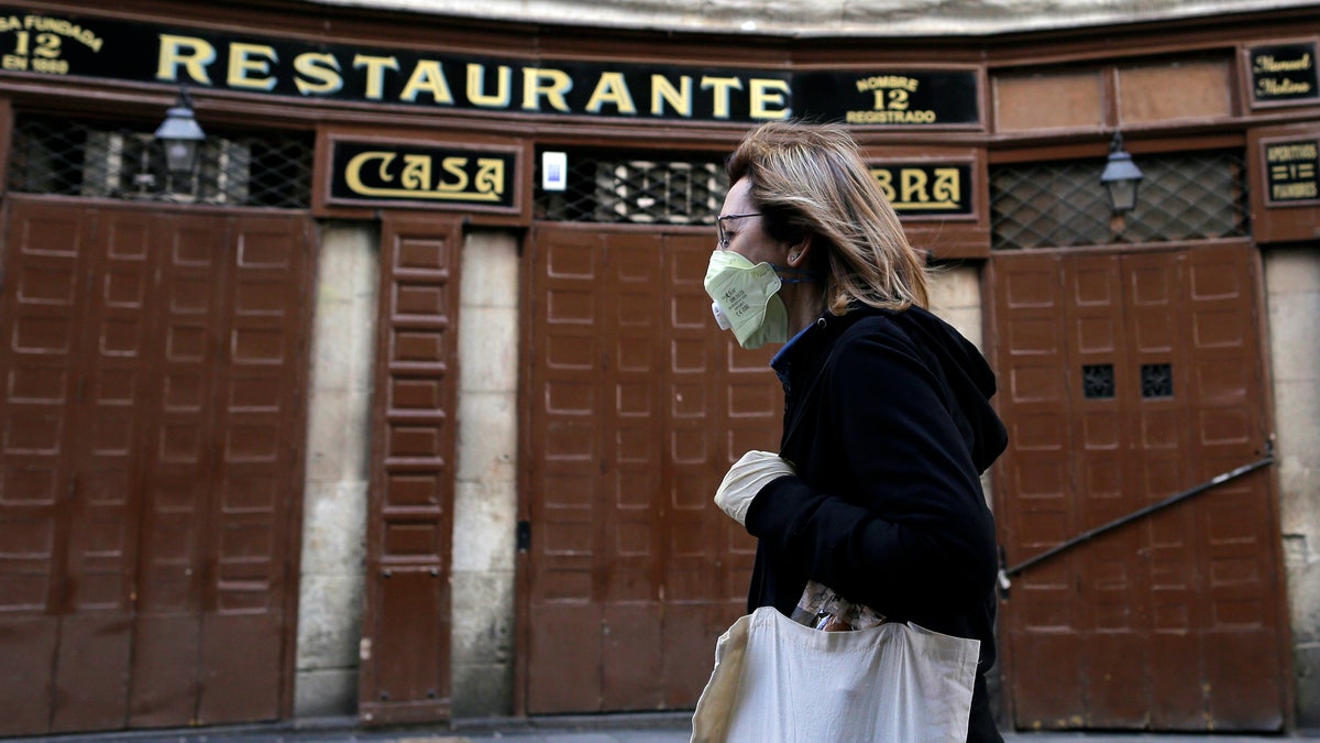 A woman wears a face mask as she walks in front of a closed restaurant in downtown Madrid, Spain, Saturday, March 14, 2020. Spanish Prime Minister Pedro Sanchez said his government will declare a two-week state of emergency on Saturday, giving itself extraordinary powers including the mobilization of the armed forces, to confront the COVID-19 outbreak. For some, especially older adults and people with existing health problems, it can cause more severe illness, including pneumonia. (AP Photo/Manu Fernandez)