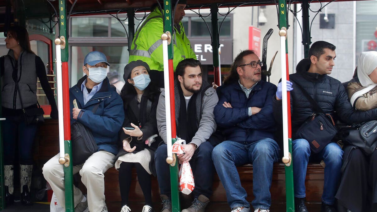 A man and woman wear masks while riding a Cable Car in San Francisco.