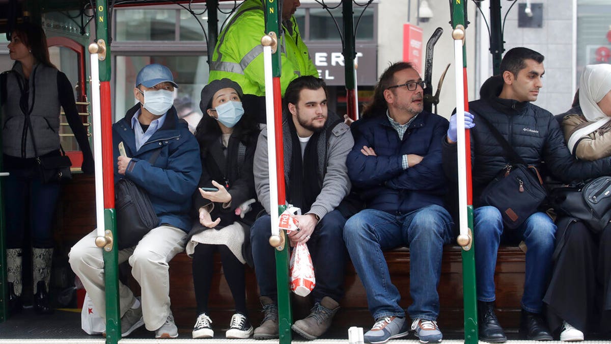 A man and woman wear masks while riding a Cable Car in San Francisco.