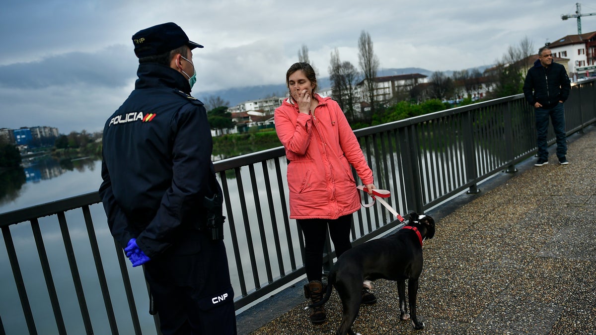 A Spanish police officer blocks the way near the border, close to the Spanish basque village of Irun, northern Spain, Tuesday, March 17, 2020. Spain is restoring border controls and severely restricting who can enter the country. Interior Minister Fernando Grande-Marlaska announced Monday that only Spaniards or residents in Spain, people who work just across the border or who have a compelling need will be allowed through. (AP Photo/Alvaro Barrientos)
