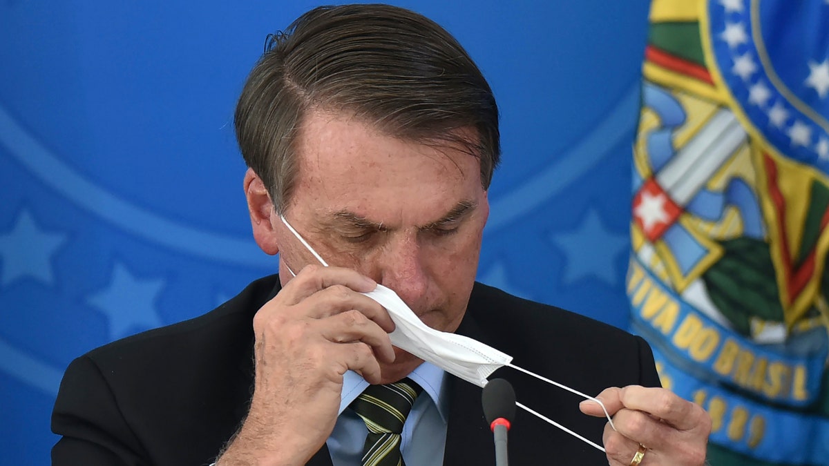 Brazil's President Jair Bolsonaro puts on a mask during a press conference on the new coronavirus at the Planalto Presidential Palace in Brasilia, Brazil, Wednesday, March 18, 2019. 