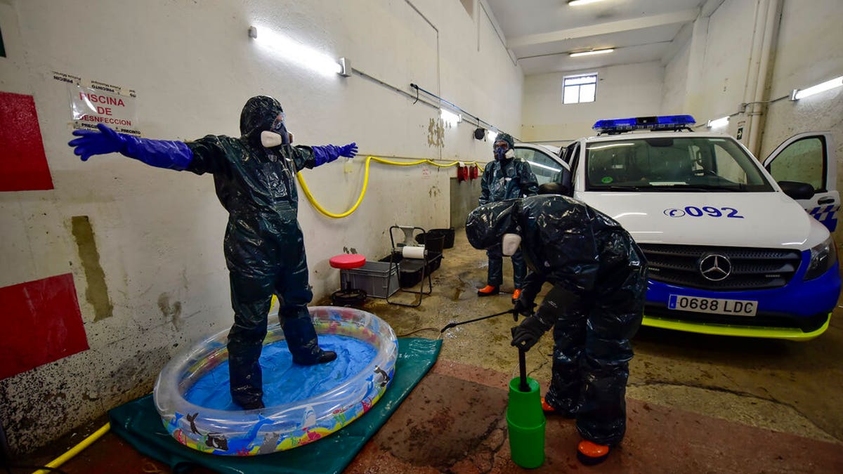 Volunteer workers of Search and Rescue (SAR) with special equipment, disinfect a volunteer while disinfecting police car at Local Police station to prevent the spread of coronavirus COVID-19, in Pamplona, northern Spain, Sunday, March 22, 2020. (AP Photo/Alvaro Barrientos)