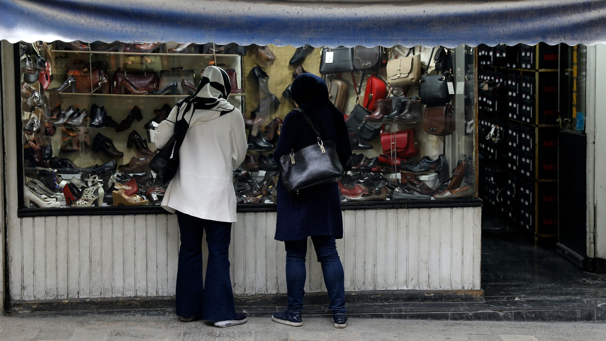 Two women look at shoes of a shop in a mostly empty street in a commercial district in downtown Tehran, Iran, Sunday, March 22, 2020. On Sunday, Iran imposed a two-week closure on major shopping malls and centers across the country to prevent spreading the new coronavirus. Pharmacies, supermarkets, groceries and bakeries will remain open. (AP Photo/Vahid Salemi)