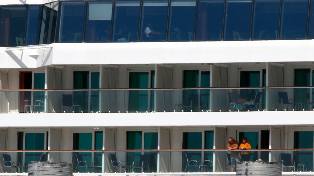 Two people look out from the Norwegian Jewel cruise ship in Honolulu on March 23. Passengers from the cruise ship that was turned away from other ports before arriving in Hawaii are being taken to Honolulu airport for chartered flights home. (AP Photo/Caleb Jones)