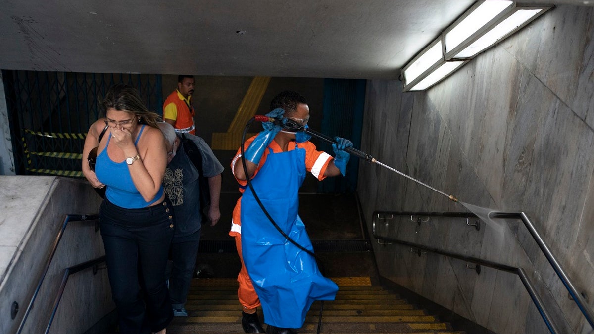 A city worker sprays disinfectant at the entrance of a metro station, which is open for service, in Rio de Janeiro, Brazil to help prevent the spread of the new coronavirus. (AP Photo/Leo Correa)