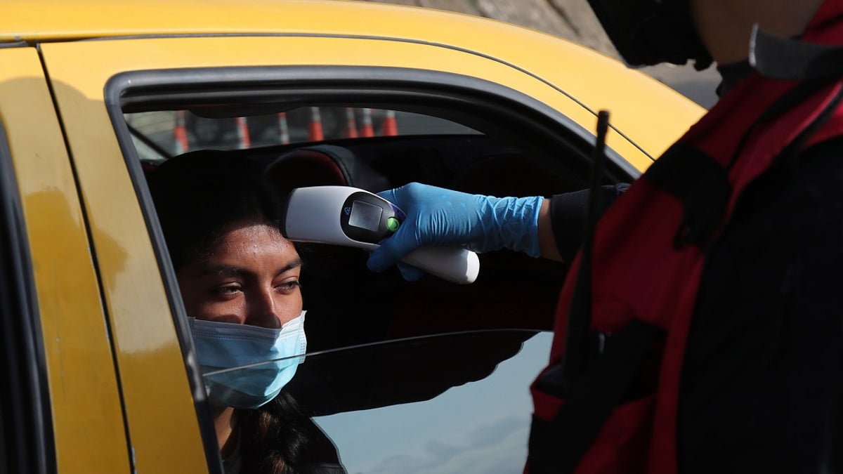 A firefighter checks the body temperature of a commuter at a toll gate, at the northern entrance to the city of Quito, Ecuador on Tuesday. Due to the worldwide spread of the new coronavirus, the government has declared a "health emergency," restricting movement to only those who provide basic services, enacting a curfew, and closing schools. (AP Photo/Dolores Ochoa)