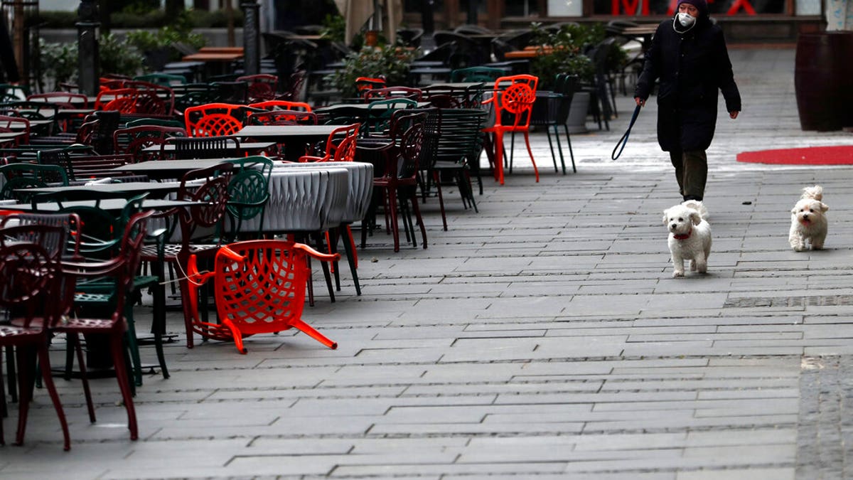 A woman walks with dogs in a deserted street amid the coronavirus outbreak in downtown Belgrade, Serbia, Thursday, March 26, 2020. 