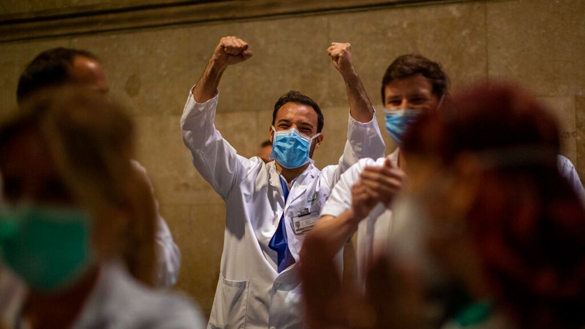 Health workers react as people applaud from their houses in support of the medical staff that are working on the COVID-19 virus outbreak at the main gate of the Hospital Clinic in Barcelona, Spain, Thursday, March 26, 2020. 