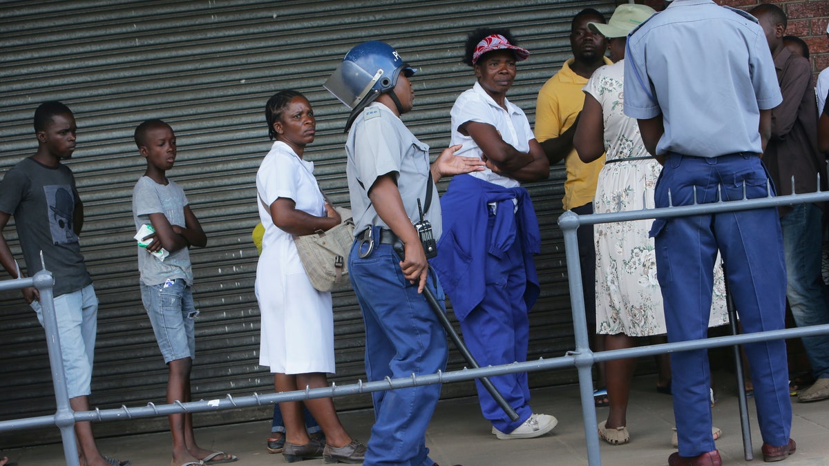 Zimbabwean police urge people to practice social distancing while in a queue to enter a supermarket in Harare, Zimbabwe, Monday, March 30, 2020. Zimbabwe went into lockdown for 21 days in an effort to curb the spread of the coronavirus. The new coronavirus causes mild or moderate symptoms for most people, but for some, especially older adults and people with existing health problems, it can cause more severe illness or death. (AP Photo/Tsvangirayi Mukwazhi)