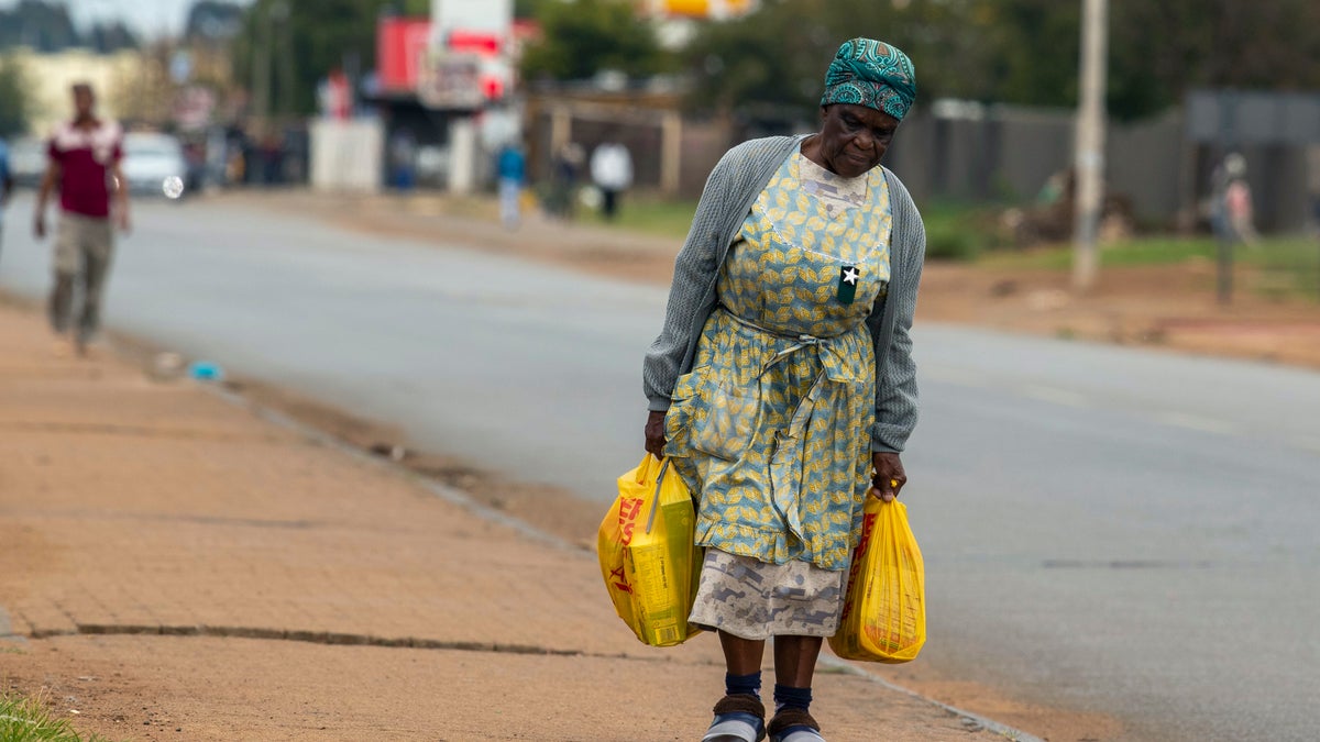 A pensioners Maria Hadebe, walks back home as she carries shopping bags filled with essential items after receiving social grant payout in Thokoza, east of Johannesburg, South Africa, Monday, March 30, 2020, as South Africa continued its nationwide lockdown for 21 days in an effort to control the spread of the coronavirus. The virus causes mild or moderate symptoms for most people, but for some, especially older adults and people with existing health problems, it can cause more severe illness or death. (AP Photo/Themba Hadebe)