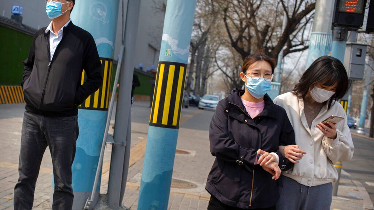 People wearing face masks wait to cross a street in Beijing, Tuesday, March 31, 2020. 