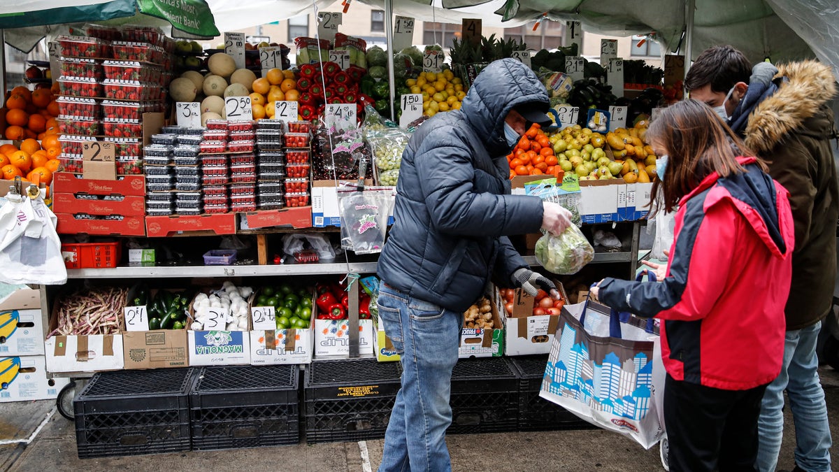 Customers shop at a fruit and vegetable street cart while wearing protective masks due to COVID-19 concerns, Monday, March 23, 2020, in New York.