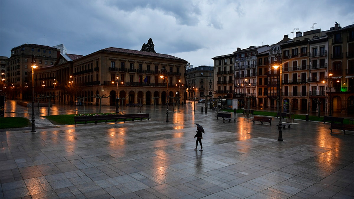 A person walks through an empty Plaza del Castillo square in the old city, in Pamplona, northern Spain, Sunday, March 15, 2020. Spain's prime minister announced a two-week state of emergency from Saturday in a bid to contain the new coronavirus outbreak. (AP Photo/Alvaro Barrientos)