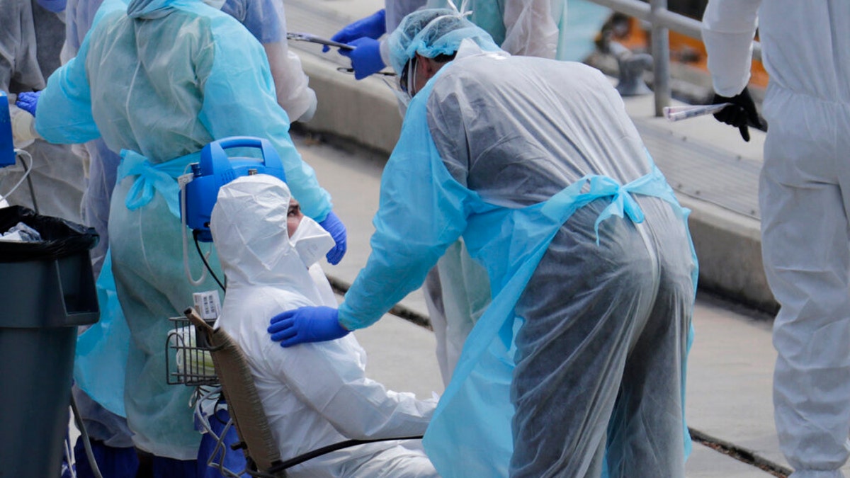 An ill crew member from the Costa Cruise ship Favolosa, left, is screened by medical personnel after arriving ashore on Thursday, March 26, at the Port of Miami.