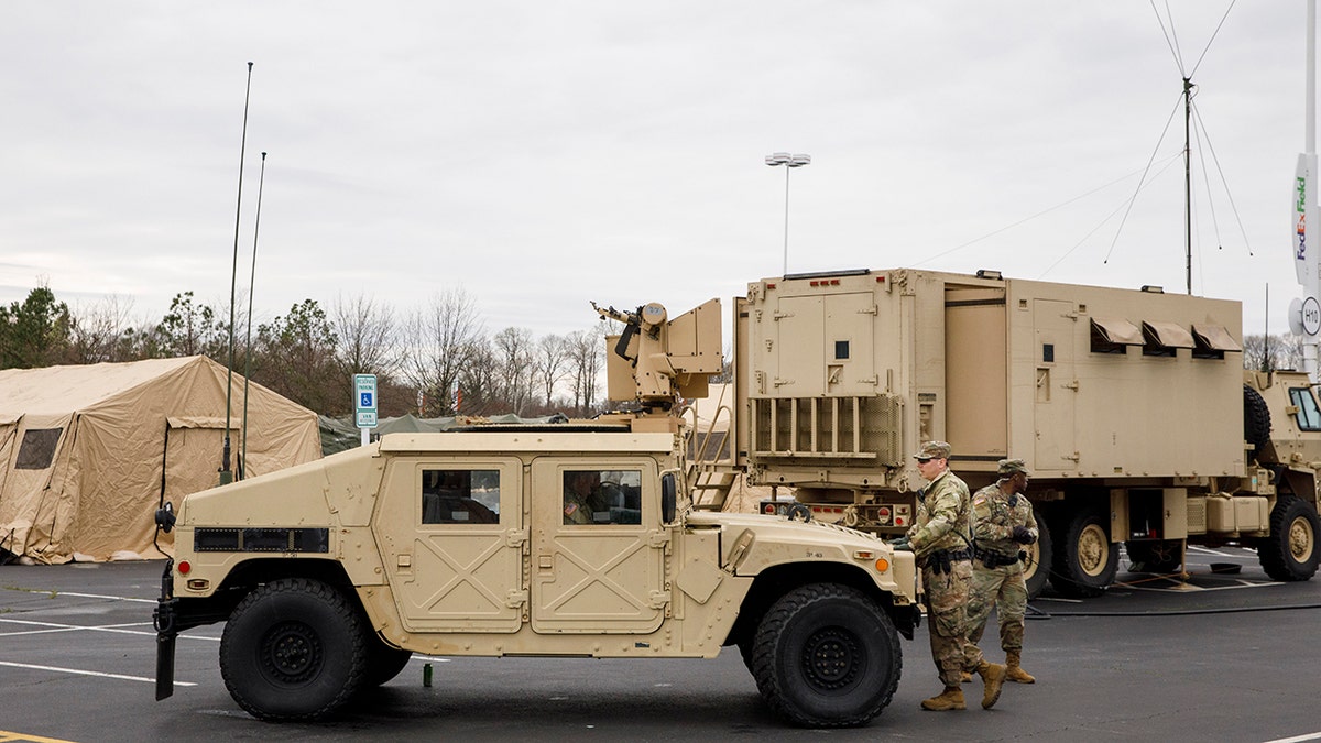 Soldiers with a security unit guard the perimeter as members of the National Guard set up tents to be used for coronavirus testing, Saturday, March 21, 2020, in a parking lot for FedEx Field in Landover, Md., outside of Washington. (AP Photo/Jacquelyn Martin)