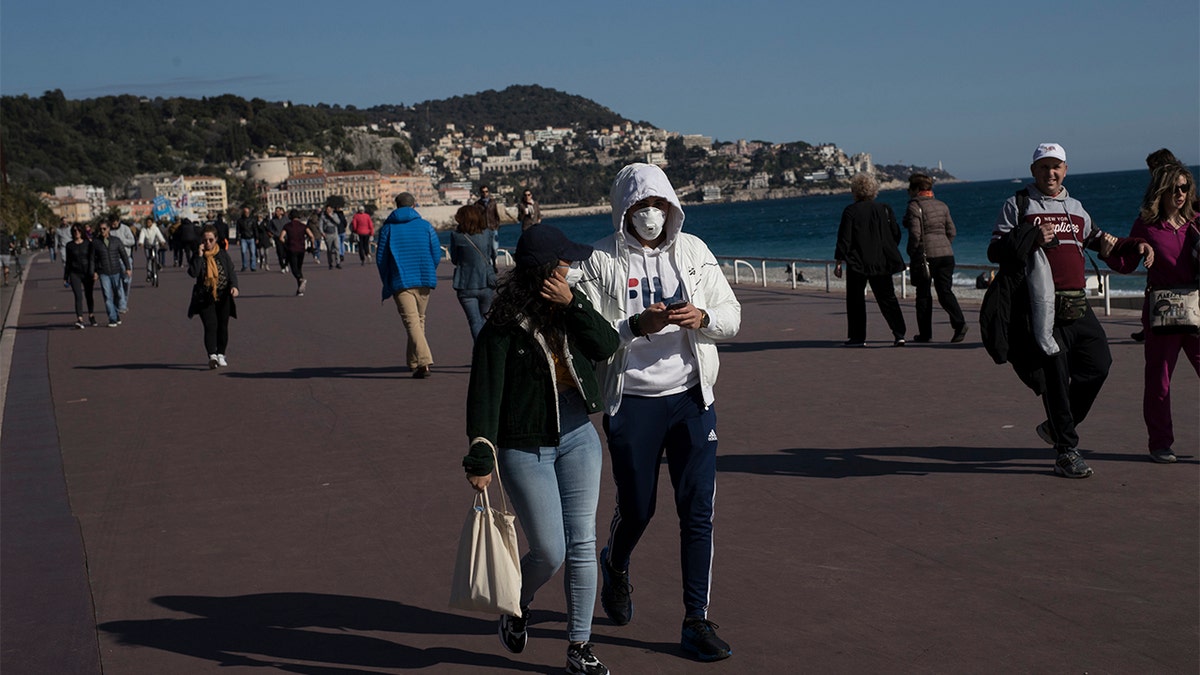 People wearing masks walk along Nice's Promenade des Anglais in Nice, southern France, Sunday, March 15, 2020. (AP Photo/Daniel Cole)