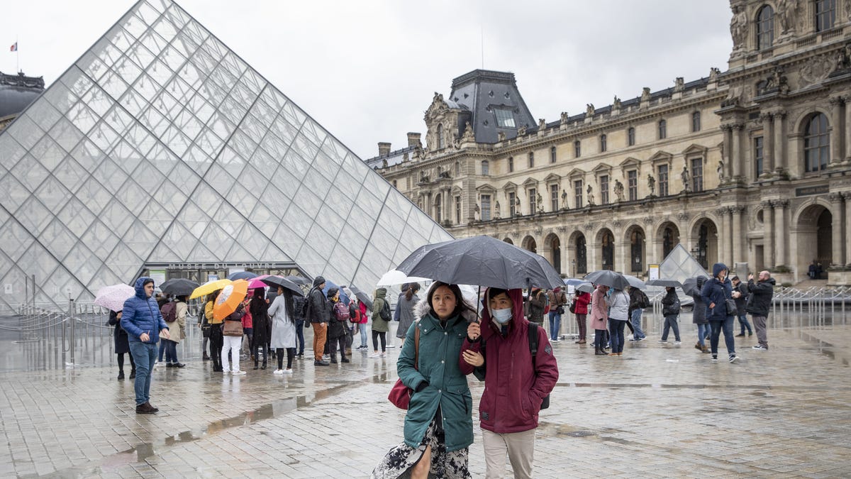 Pedestrians wearing face masks beneath an umbrella outside the Louvre Museum on March 2. The museum was closed for a few days due to staff worries over the coronavirus outbreak.