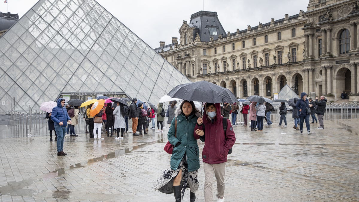 Pedestrians wearing face masks beneath an umbrella outside the Louvre Museum on March 2. The museum was closed for a few days due to staff worries over the coronavirus outbreak.