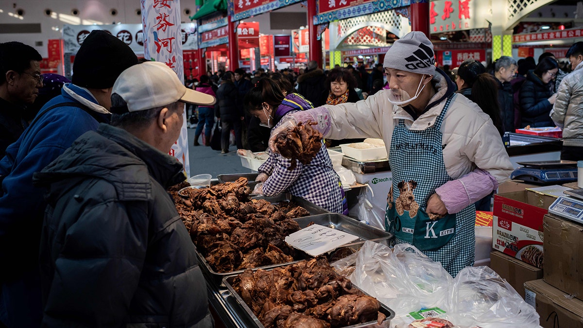 A vendor sells meat to customers at a market in Beijing on Jan. 15.
