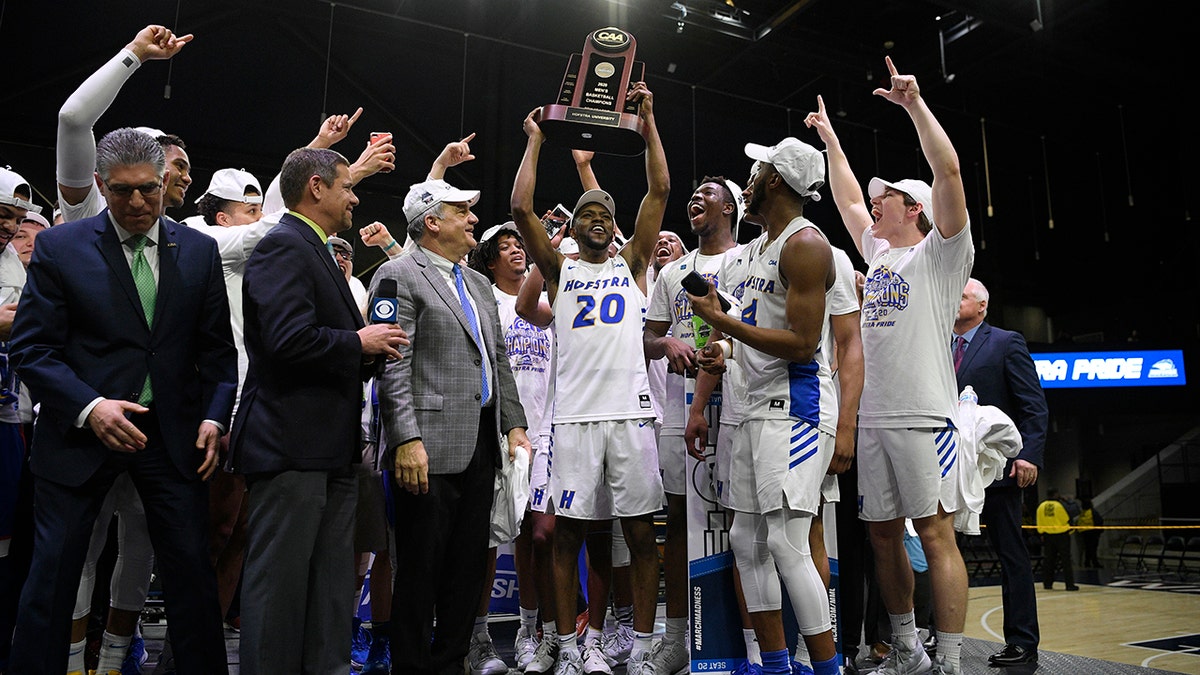Hofstra guard Jalen Ray (20) and others raise the trophy after defeating Northeastern in an NCAA college basketball game for the championship of the Colonial Athletic Association men's tournament Tuesday, March 10, 2020, in Washington. Hofstra won 70-61. (AP Photo/Nick Wass)