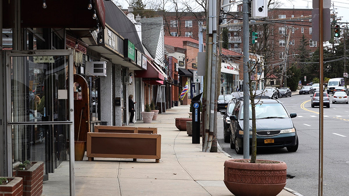 A solitary woman checks her cellphone on a normally busy North Avenue inside what's called a "containment area" in New Rochelle, N.Y., Wednesday, March 11, 2020. State officials on Tuesday called for closing schools, houses of worship and any other spaces were large numbers of people gather within a 1-mile radius (1.6 kilometers) of a point near a synagogue where an infected person had attended events. (AP Photo/Chris Erhmann)